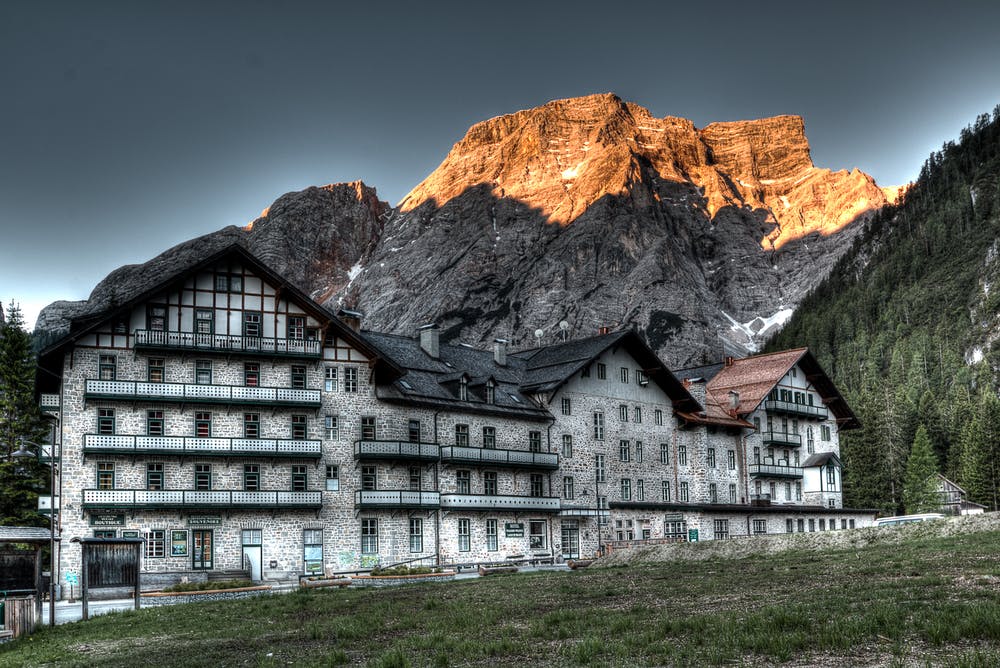 Vista di un grande rifugio con dietro delle montagne rocciose e illuminate dal sole