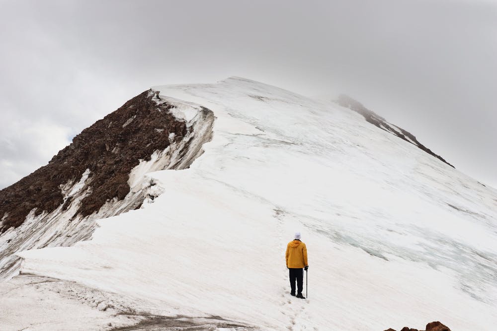 Vista della cima di una montagna innevata e un ragazzo vestito di giallo di spalle