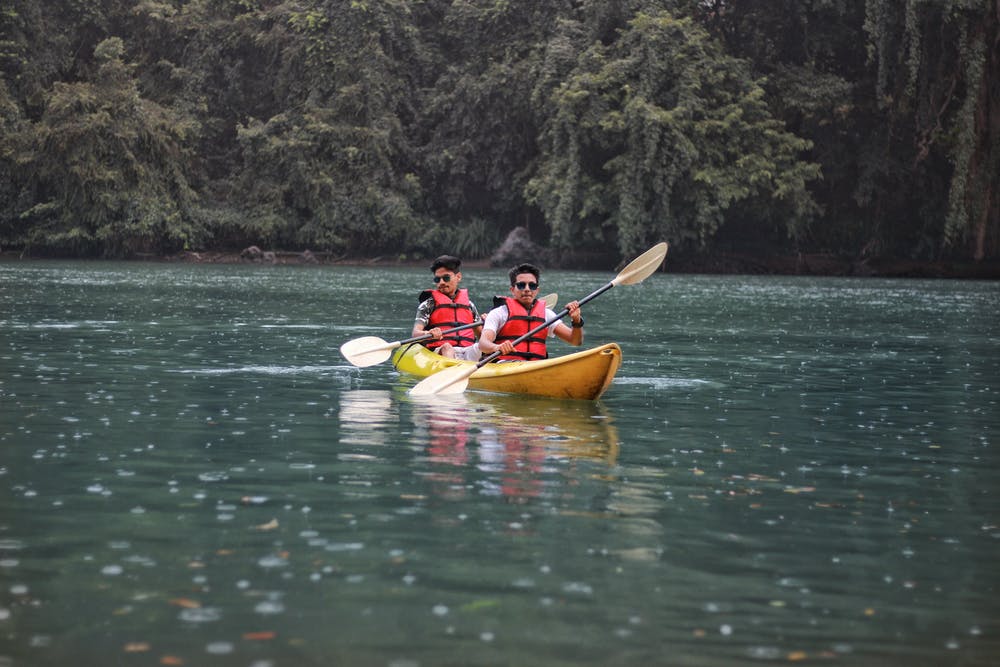 Foto di due ragazzi mentre fanno canoa in mezzo ad un lago circondato da alberi verdi