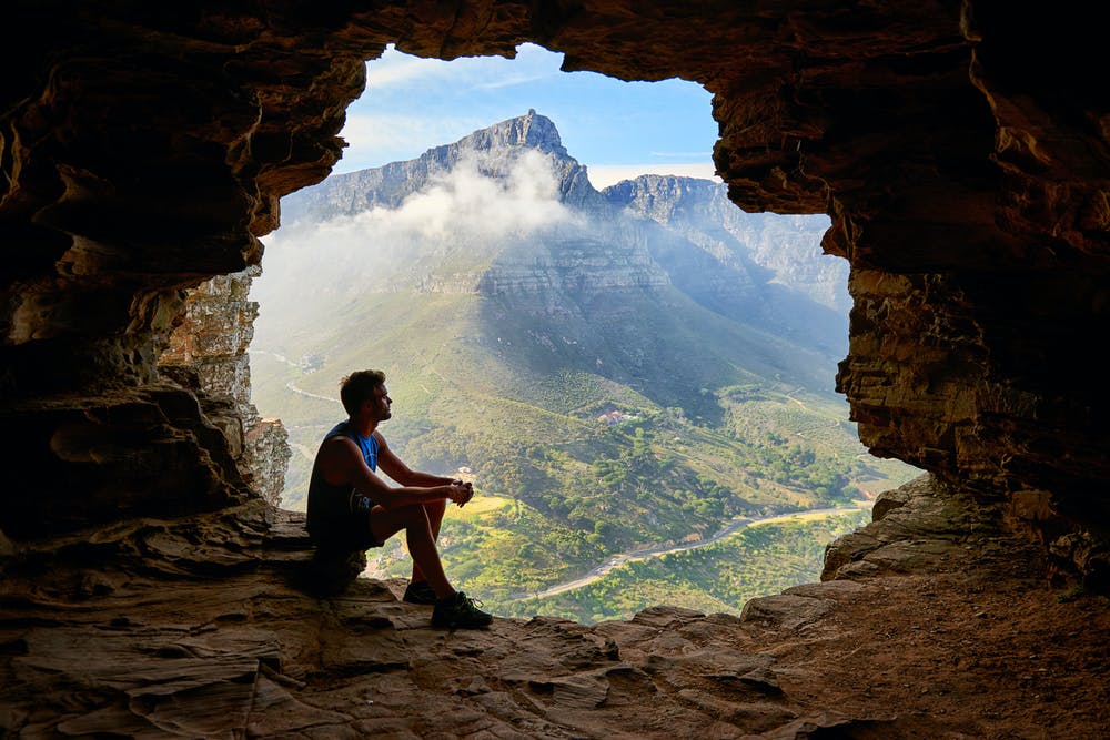 Foto di un ragazzo dentro una grotta con vista sulle montagne verdi