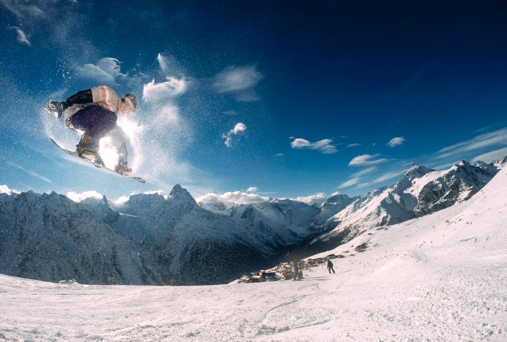 Vista montagne con la neve e una pista da scii con un ragazzo che fa snowboarding