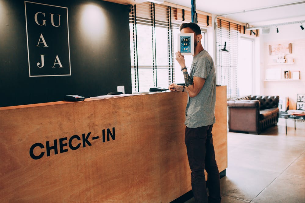 Foto di un ragazzo al check-in di un hotel mentre si copre il viso con un volantino