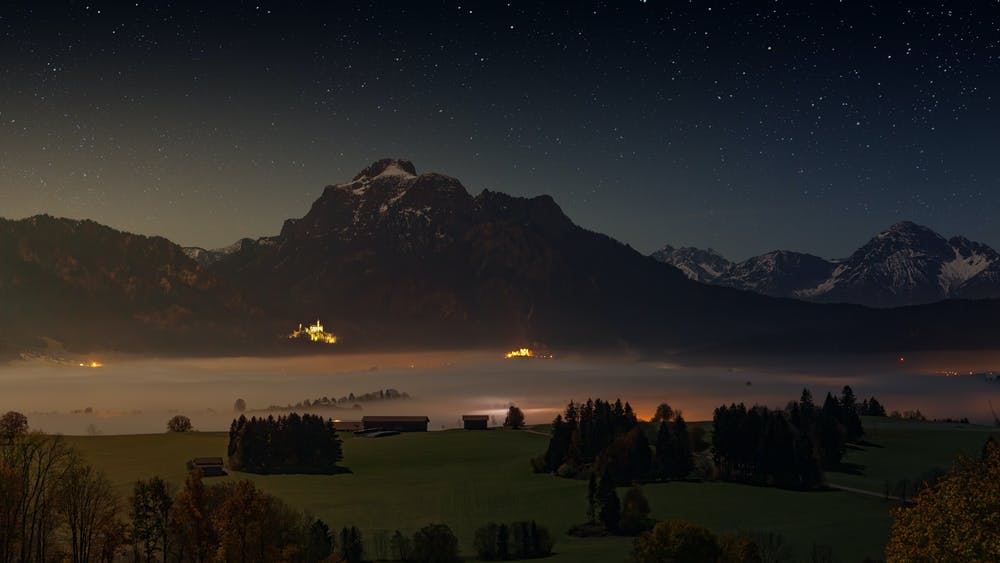 Vista notturna di alberi che contornano dei rifugi alpini e delle montagne