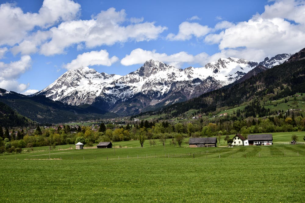 Vista montagne con neve che si affacciano su una collina verde con delle abitazioni