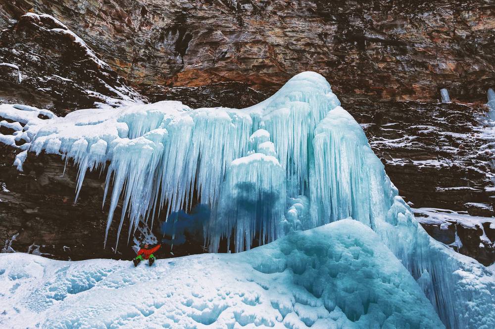 Vista montagna con chiazze di neve ed una cascata di neve ghiacciata con un ragazzo davanti