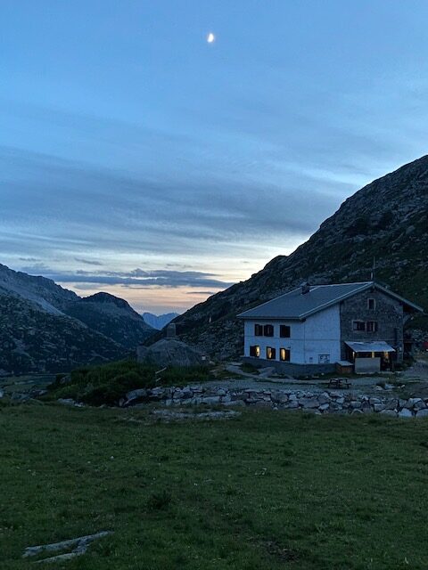 Vista di un rifugio di fronte a delle montagne con un cielo serale