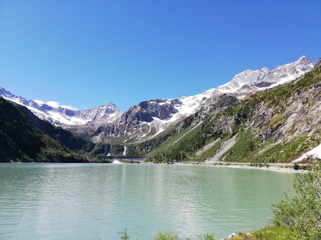 Vista di un lago limpido circondato da montagne verdi e altre coperte di neve