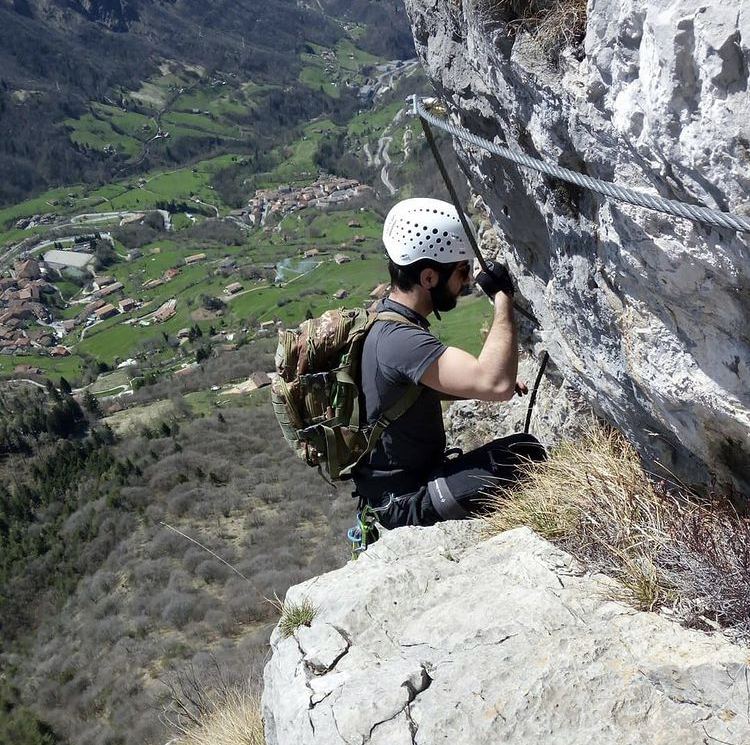 Vista dall'altro di un ragazzo che si arrampica sulla montagna e in sottofondo delle colline verdi contraddistinte da abitazioni sparse