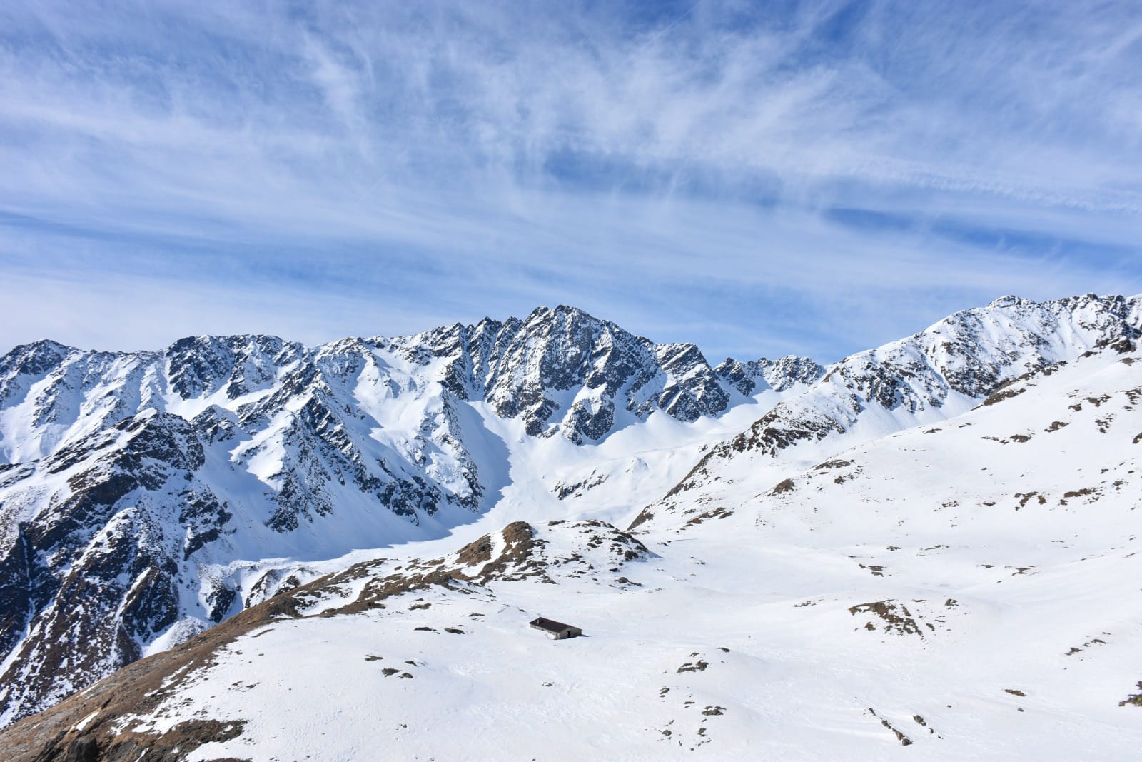 Vista di montagne completamente innevate con un'unica abitazione in mezzo alla neve, un cielo limpido e poco nuvoloso